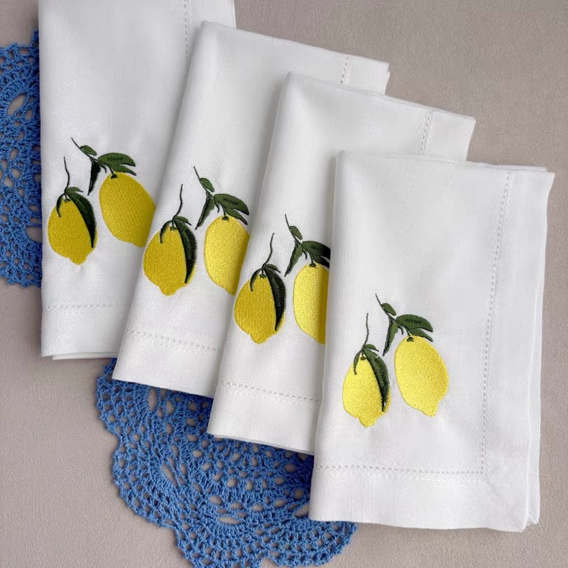 Four white embroidered lemon napkins arranged for textile-first tablescaping