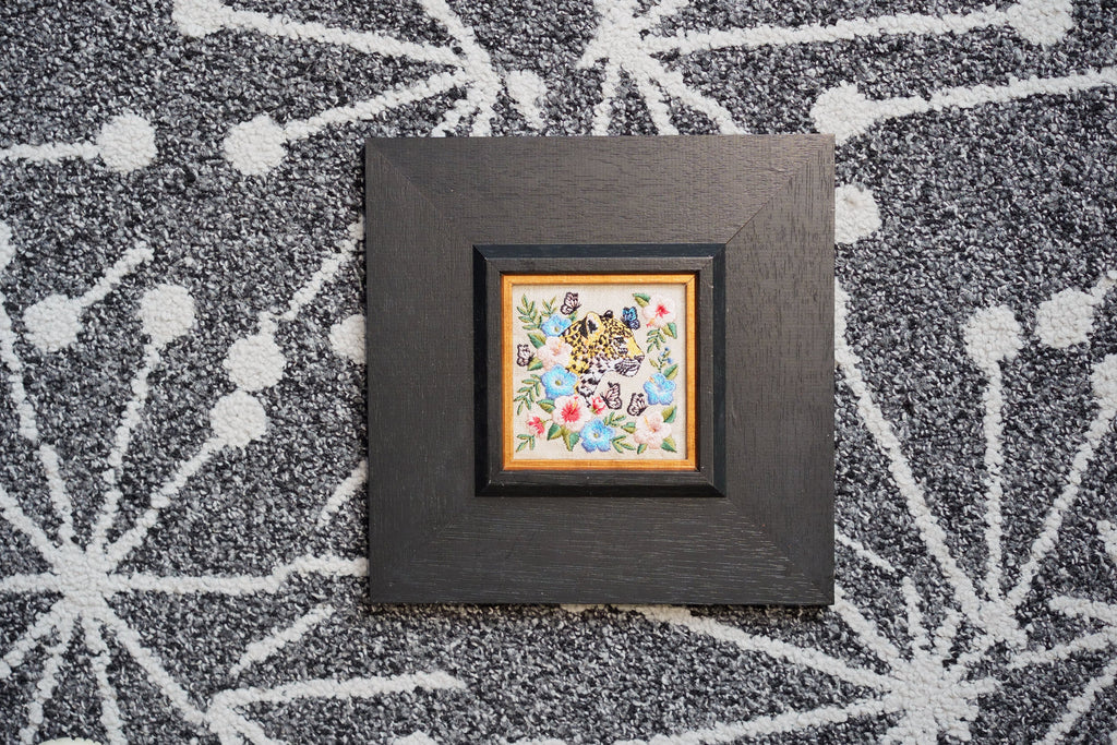 A powerful leopard emerges from a garden of delicate blooms and fluttering butterflies, capturing the timeless wisdom of the