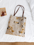 Golden Reverie floral jacquard tote with brown shoulder handles laid flat on white bedding.