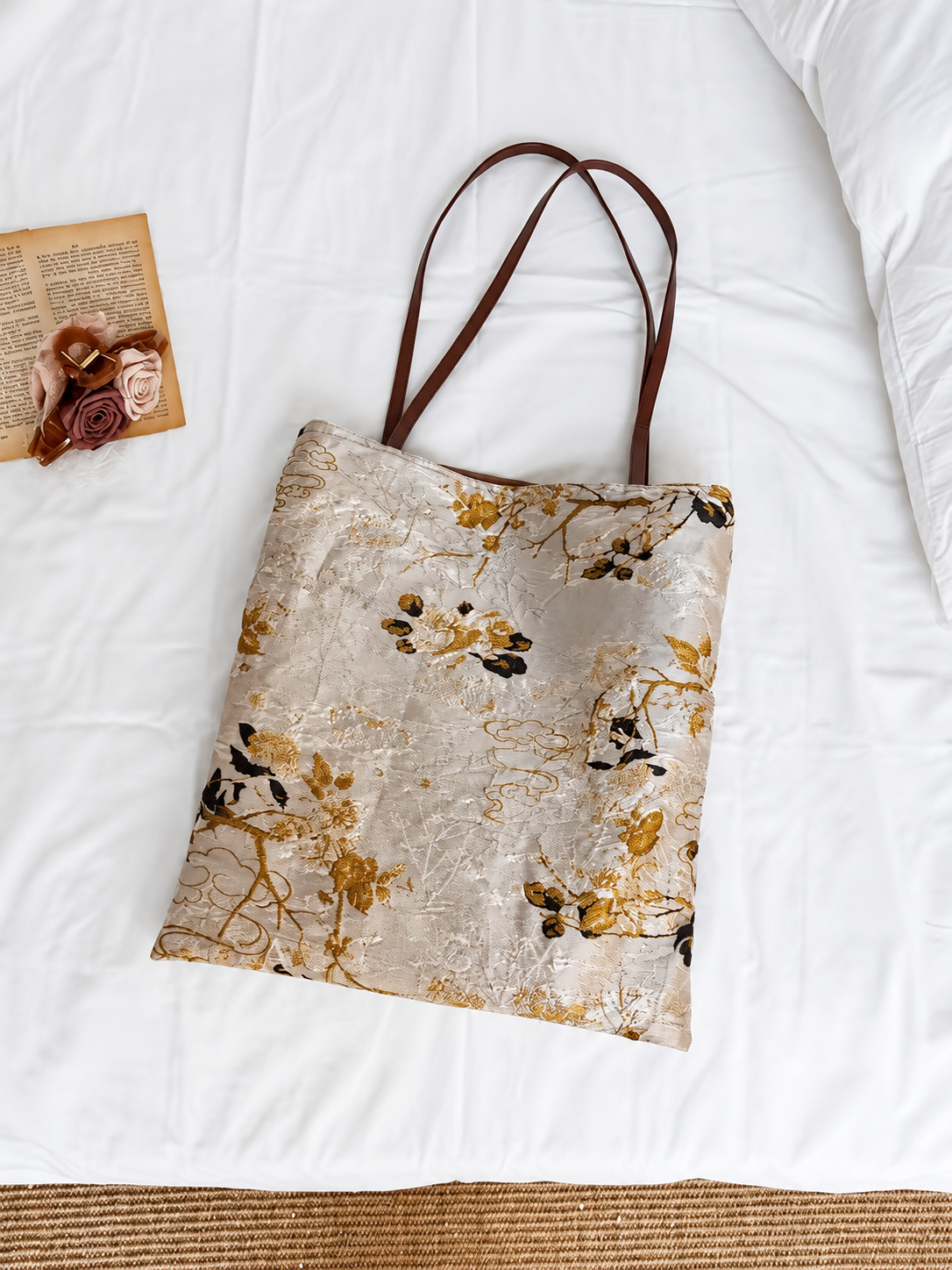 Golden Reverie floral jacquard tote with brown shoulder handles laid flat on white bedding.