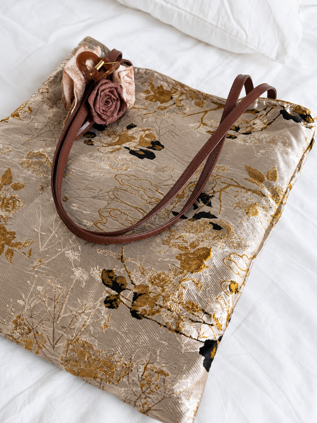 Close-up of Golden Reverie tote showing gold and dark floral motifs, brown handles and a fabric rose accessory.