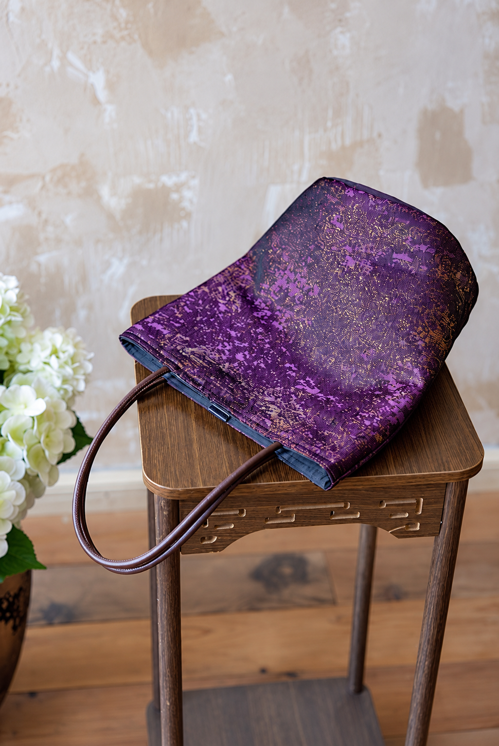 Violet Dusk purple jacquard bucket bag laid on a wooden stool with brown handles extending over the edge.