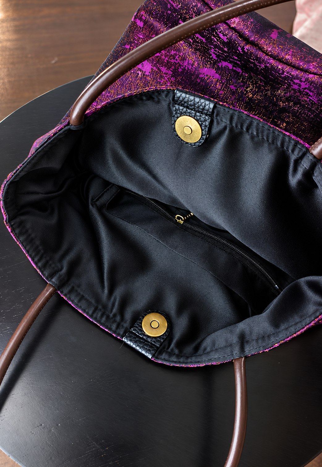 Inside the Violet Dusk bucket bag, showing black lining, a zip pocket and gold-tone magnetic closure.