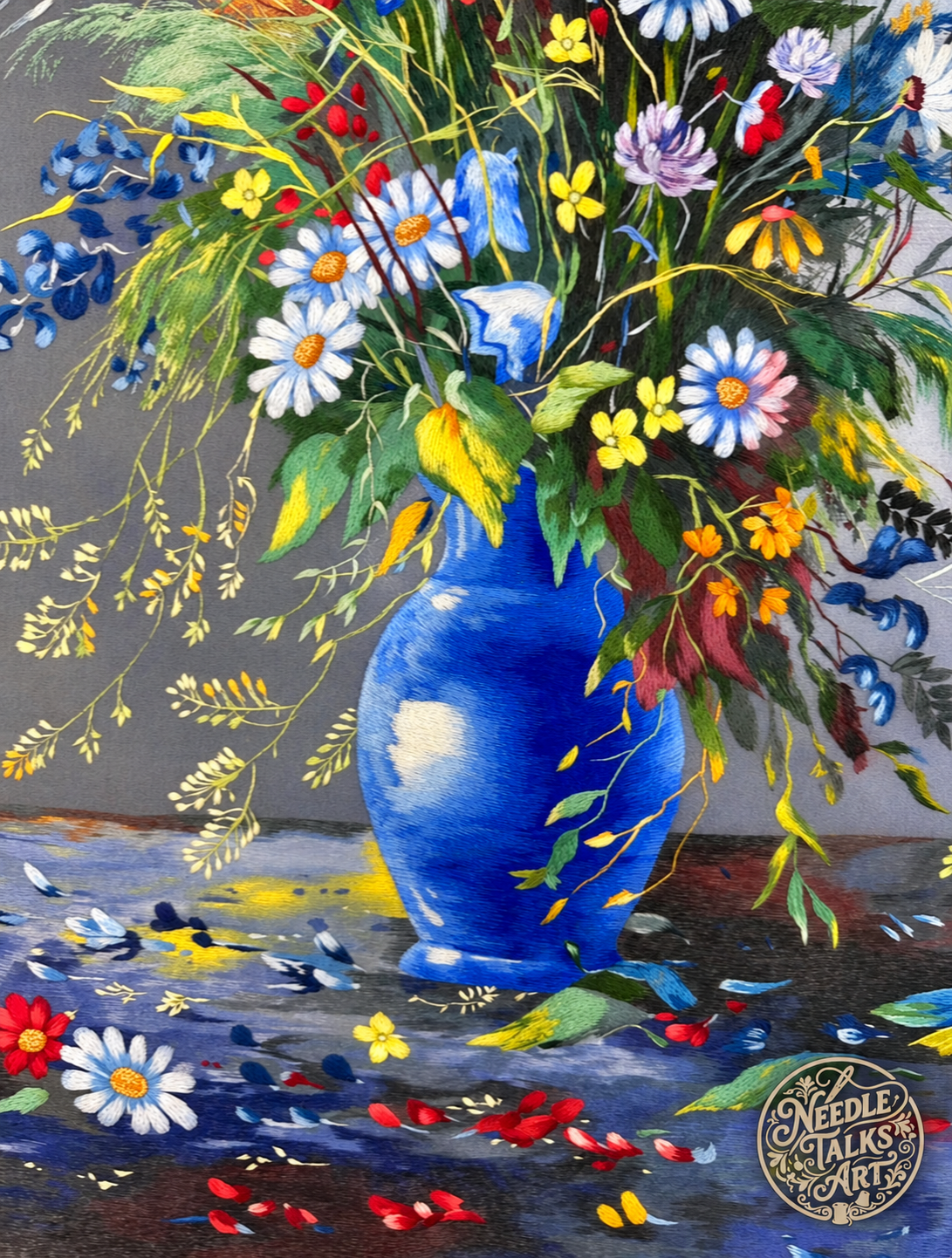 Detail of Where Wildflowers Gather embroidery showing a blue vase, daisies and scattered petals.