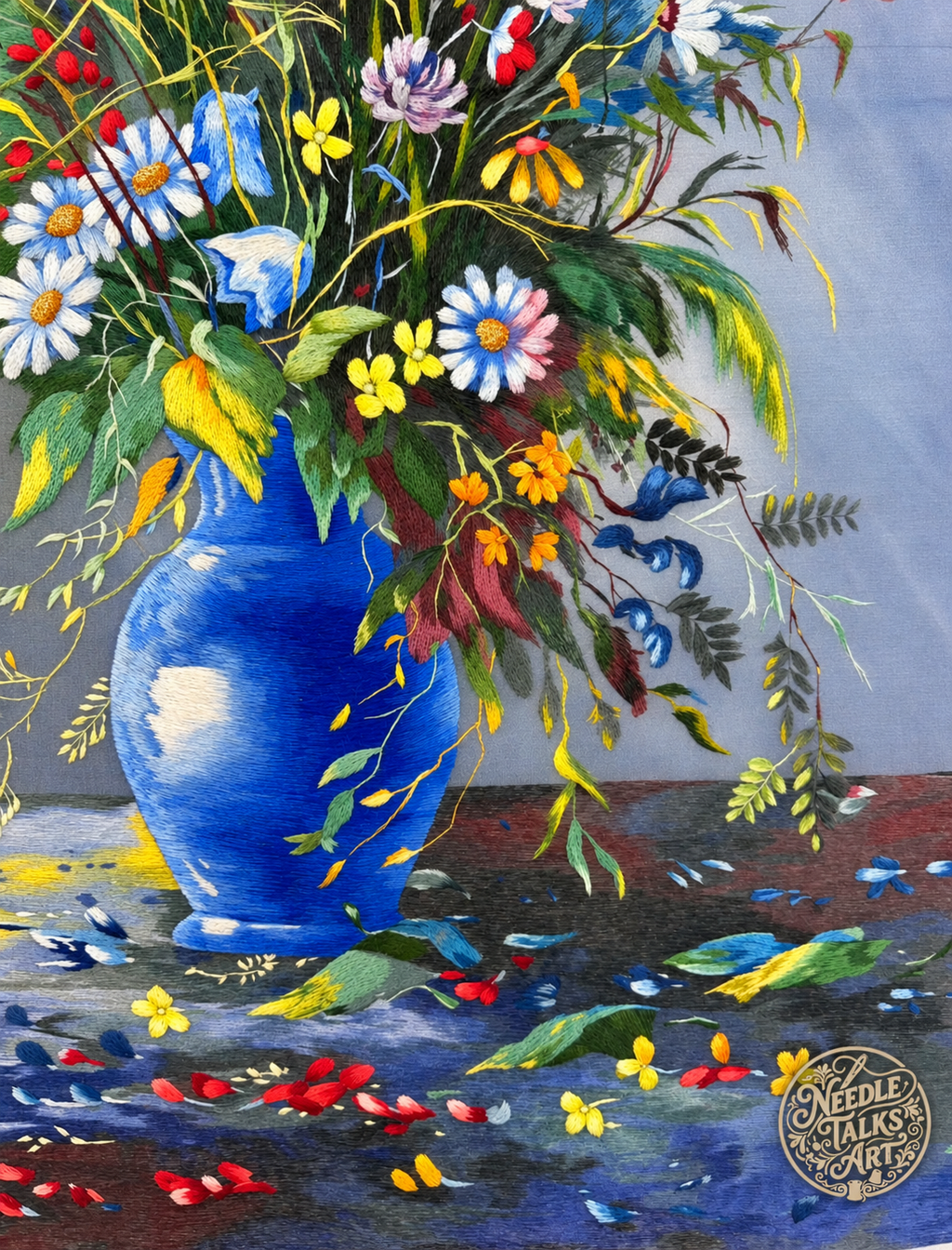 Close-up of silk stitching in the blue vase, trailing foliage and colorful flowers of Where Wildflowers Gather.