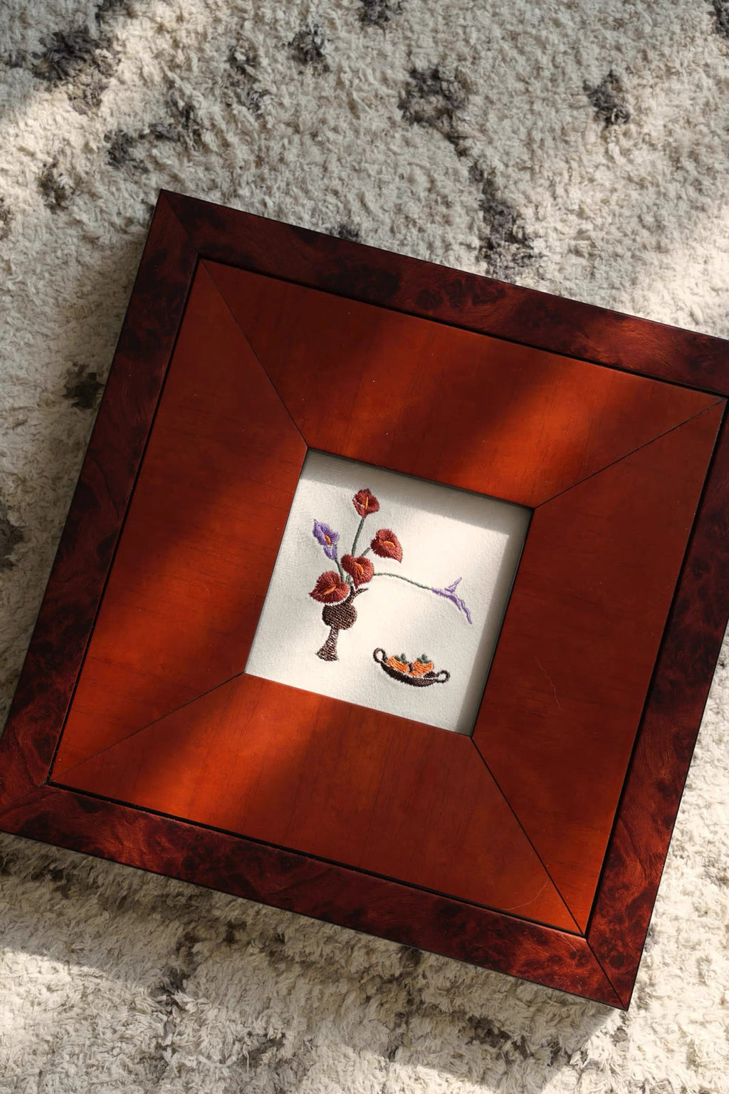 A top-down lifestyle shot of a square, dark reddish-brown solid wood picture frame resting on a white lace runner. The frame