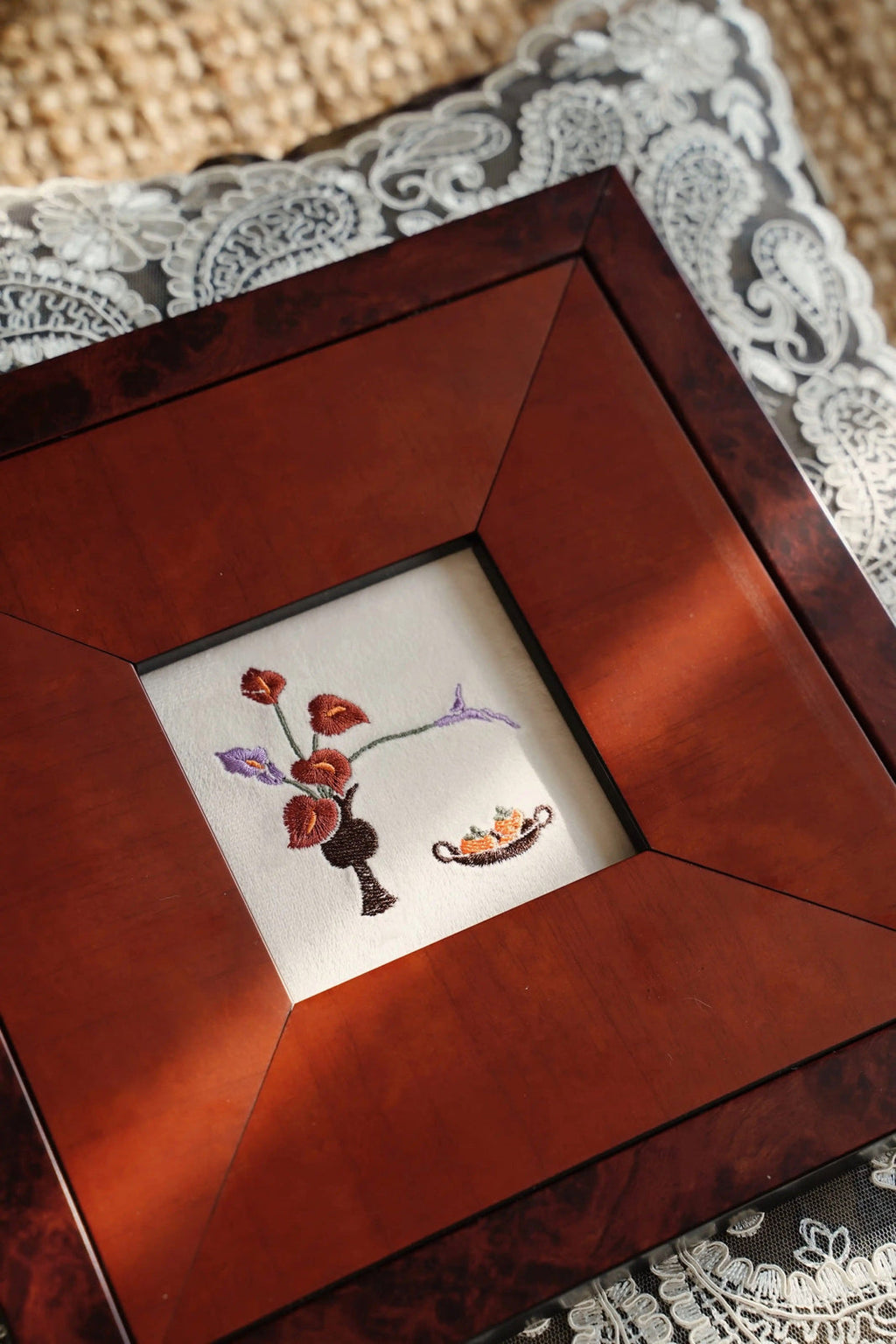 A perspective shot of the "Everlasting Bliss" embroidery frame resting on a textured cream carpet. Sunlight casts a shadow ac
