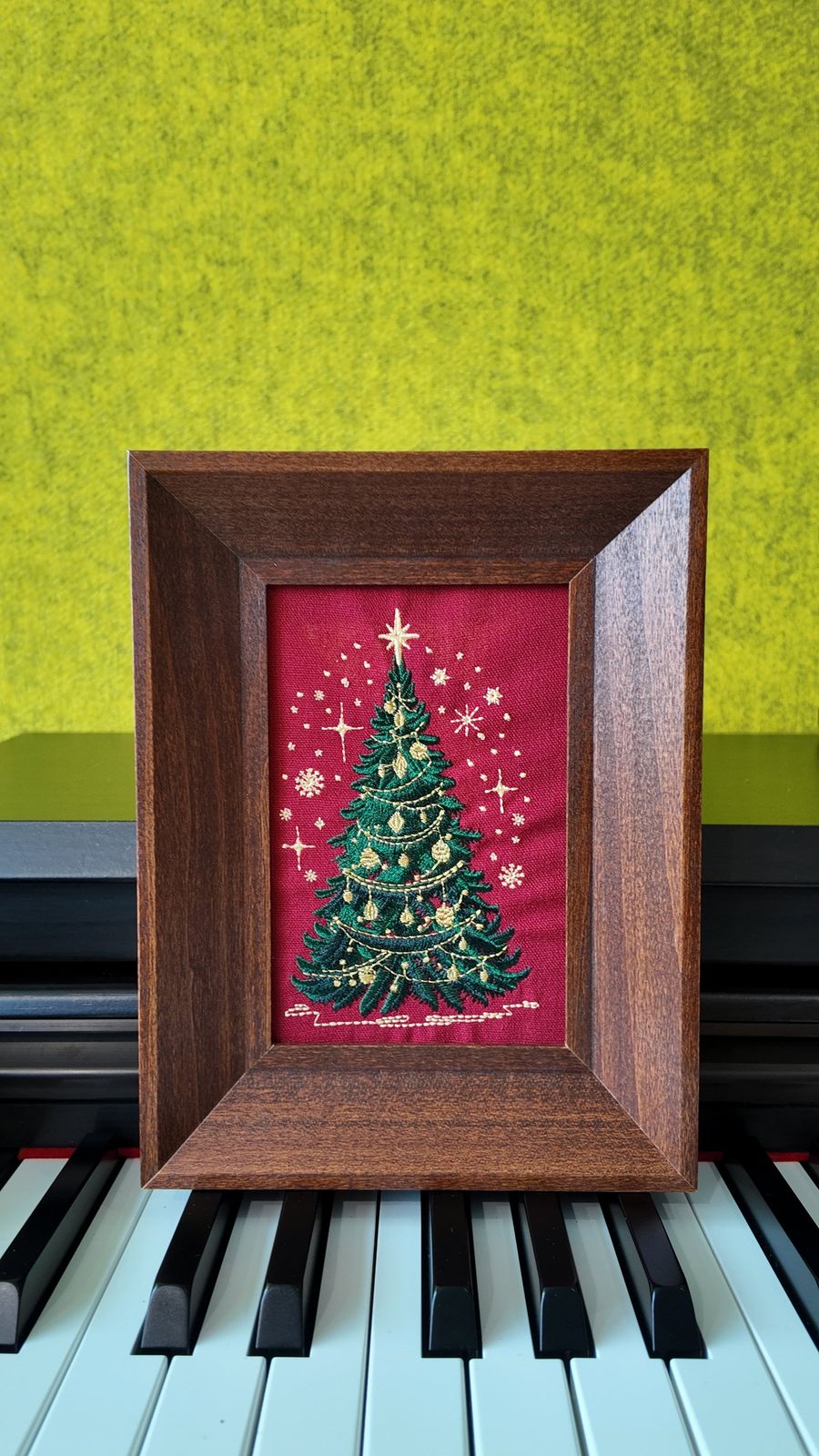 Brown framed Christmas tree embroidery displayed on a piano