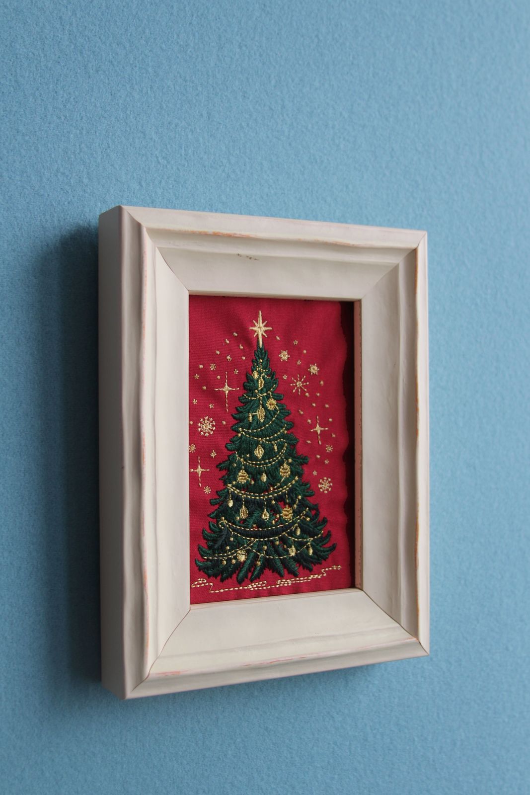 Angled view of Christmas tree embroidery in a white wood frame