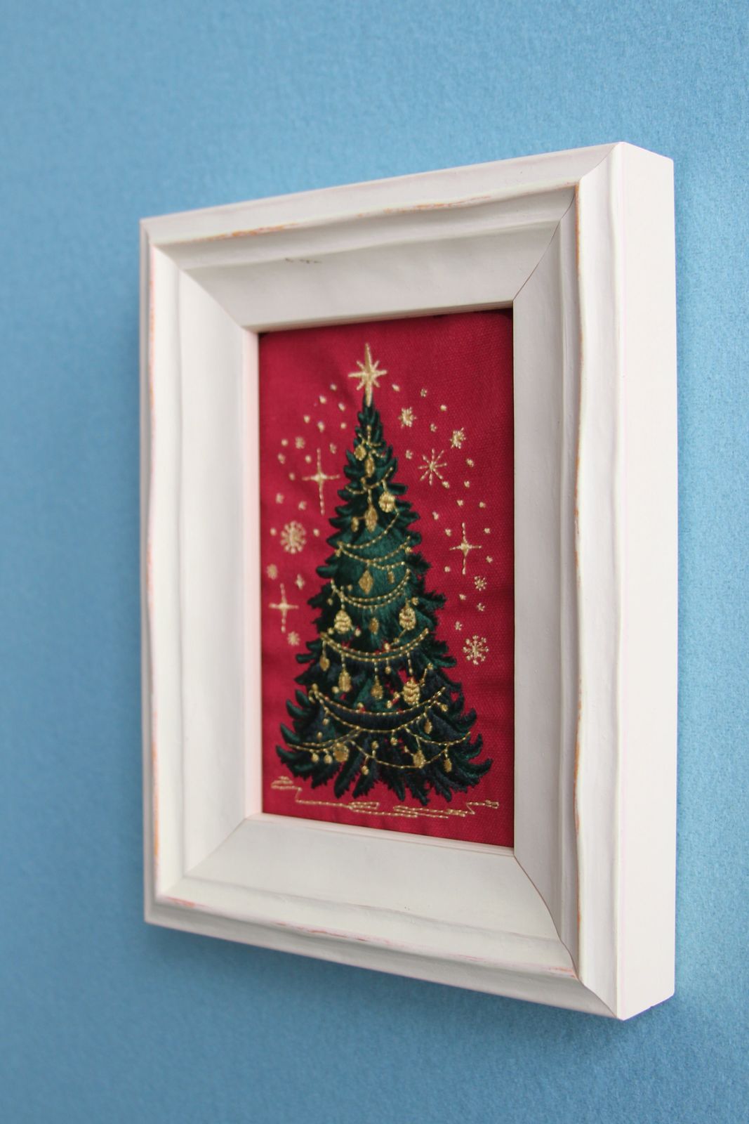 Side view showing the depth of the white wood frame and gold-thread Christmas embroidery