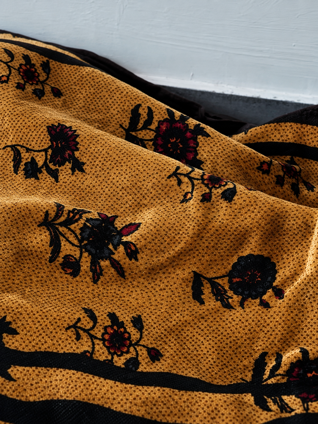 Close-up of golden mulberry silk velvet with black and burgundy floral motifs and black border stripes.