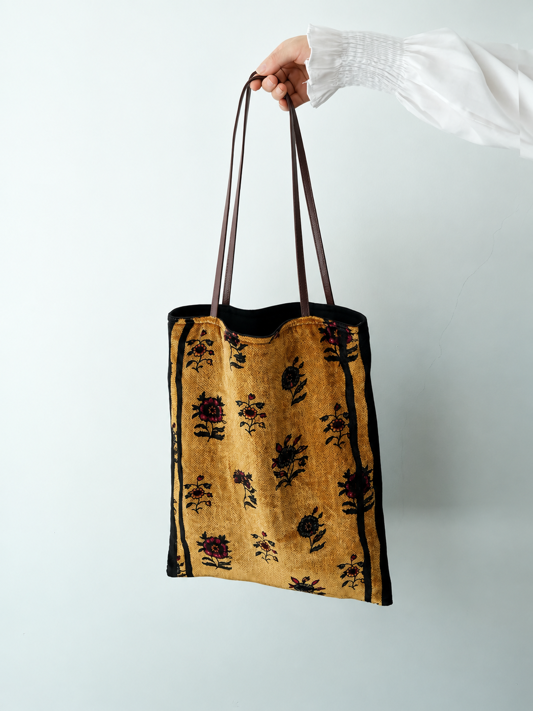 Full view of a golden floral silk velvet tote bag with its long brown straps held upright.