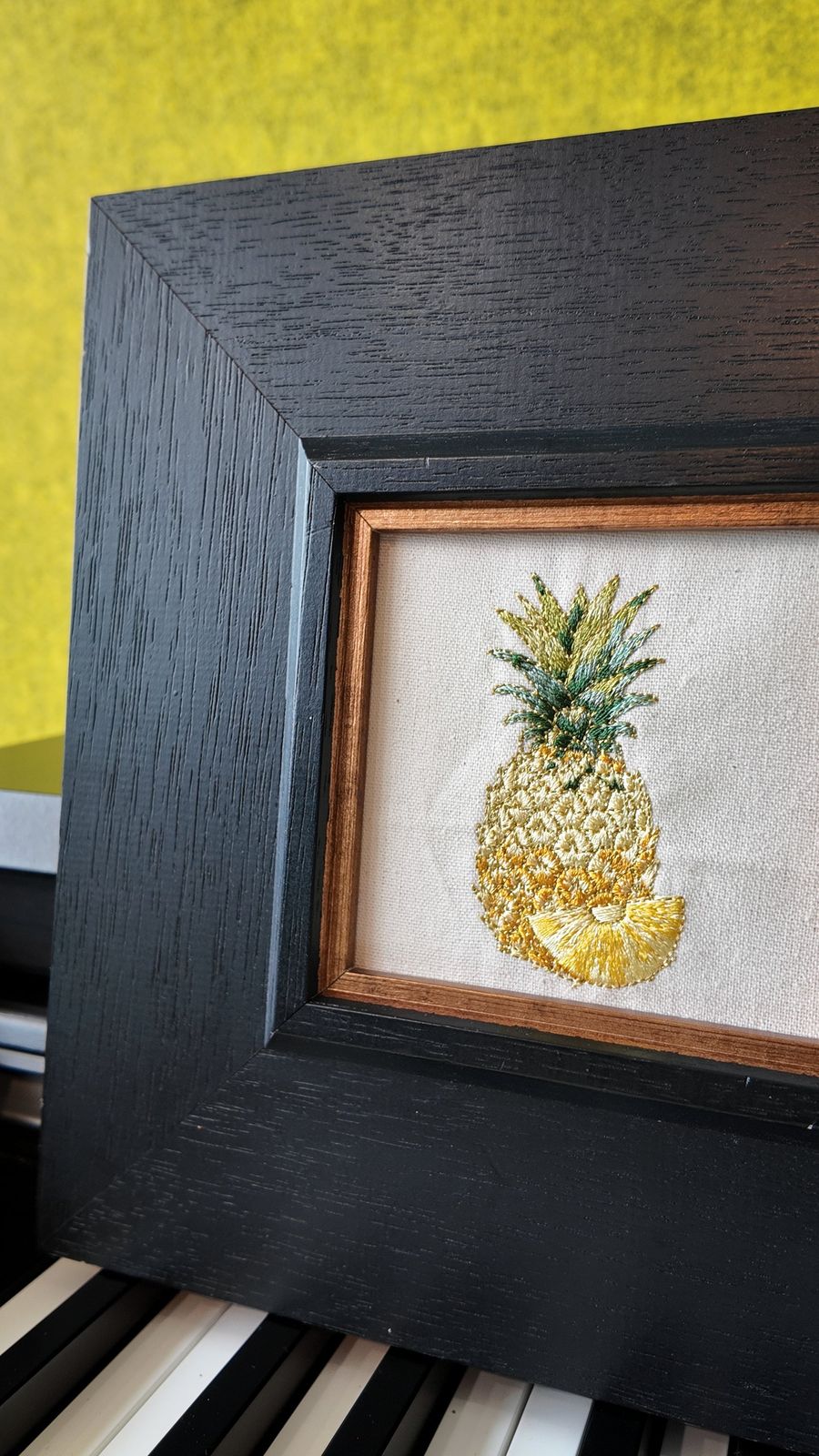 Close view of shimmering gold-thread pineapple embroidery and black wood frame