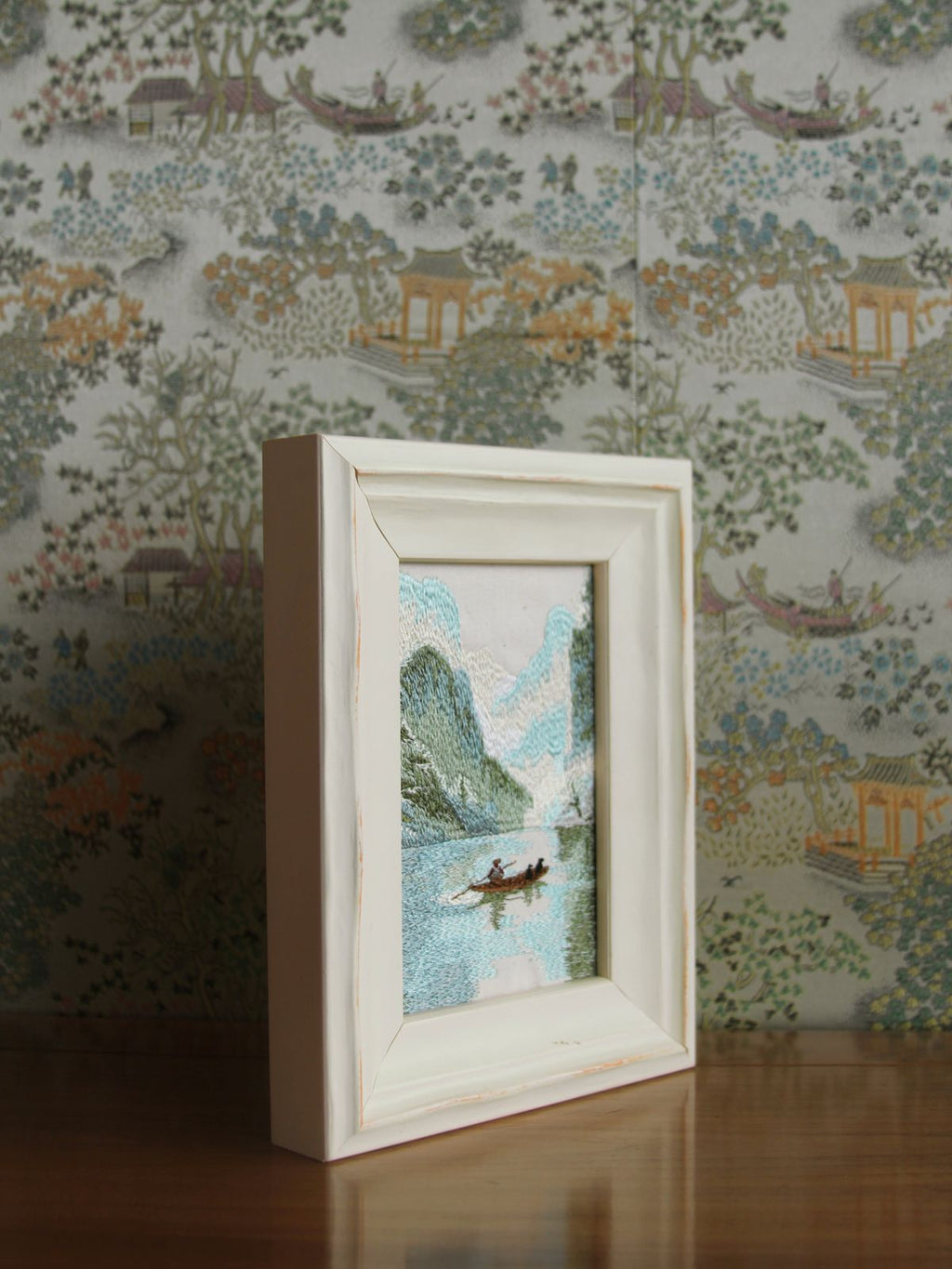 Angled tabletop view of Guilin river embroidery in a white wood frame