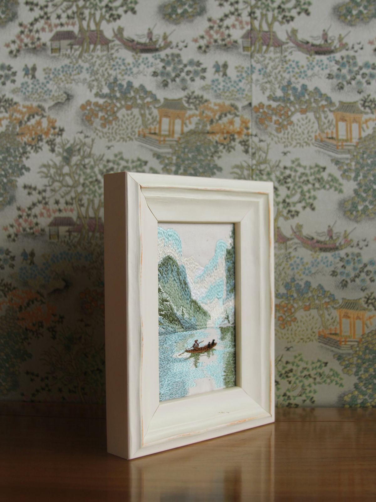 Angled tabletop view of Guilin river embroidery in a white wood frame