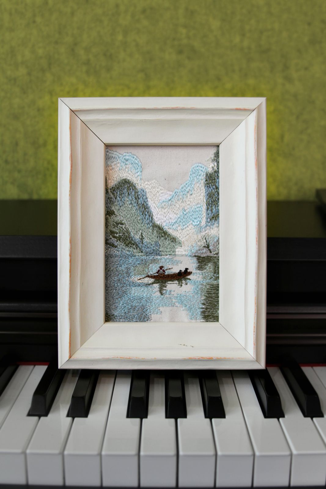Guilin karst landscape embroidery in a white wood frame displayed on a piano