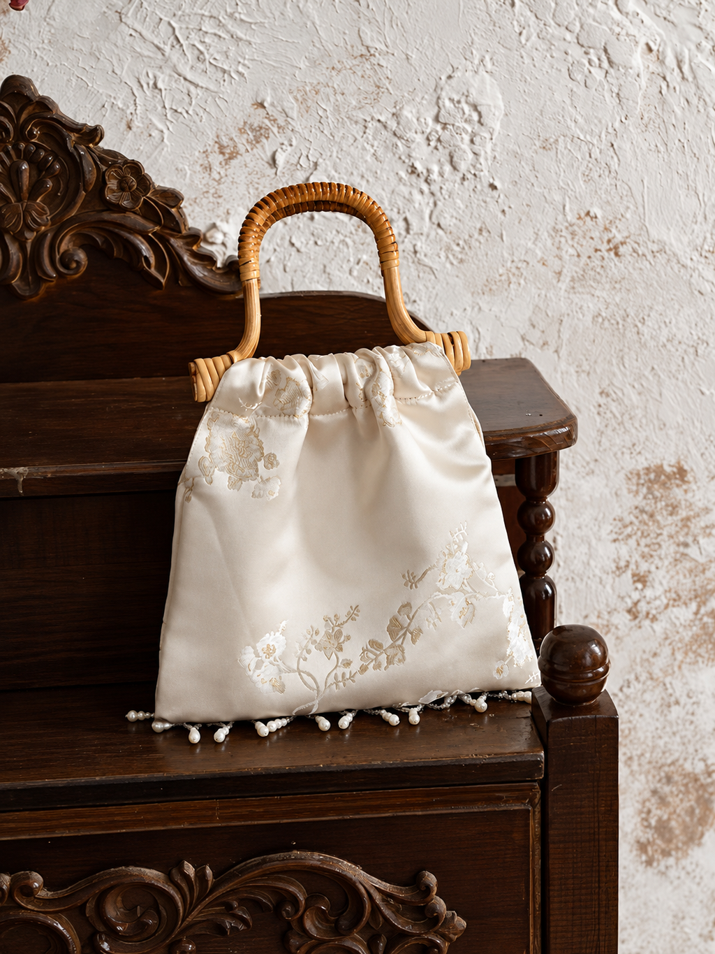 Ivory plum blossom jacquard handbag displayed on carved dark wood furniture.