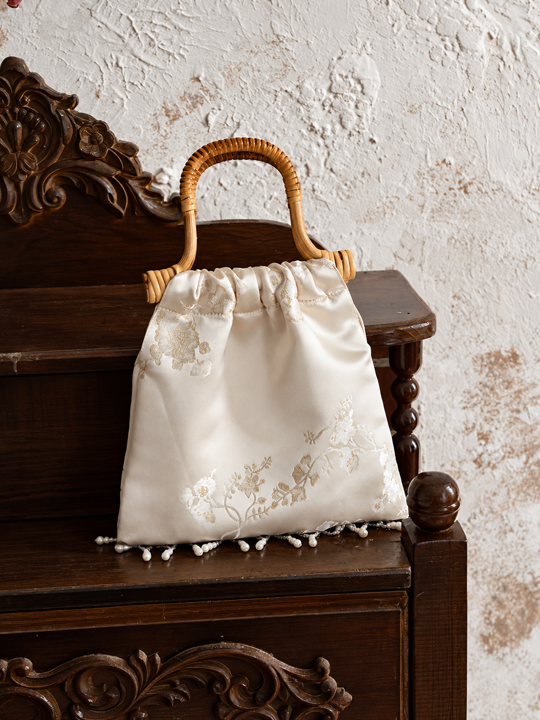 Ivory plum blossom jacquard handbag displayed on carved dark wood furniture.