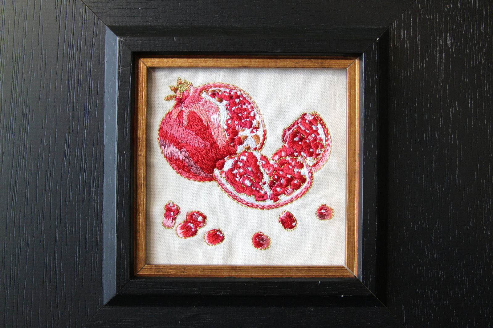 Close view of red pomegranate embroidery with shimmering gold-thread details