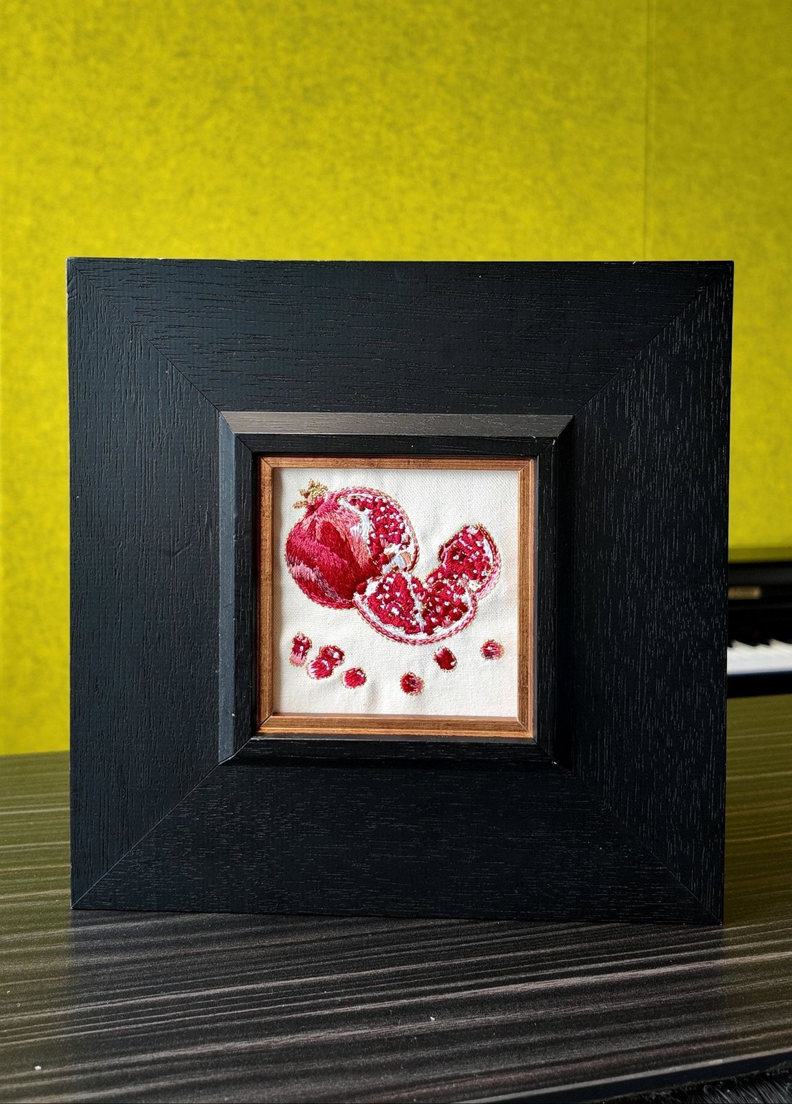 Jeweled pomegranate embroidery in a square black wood frame, front view