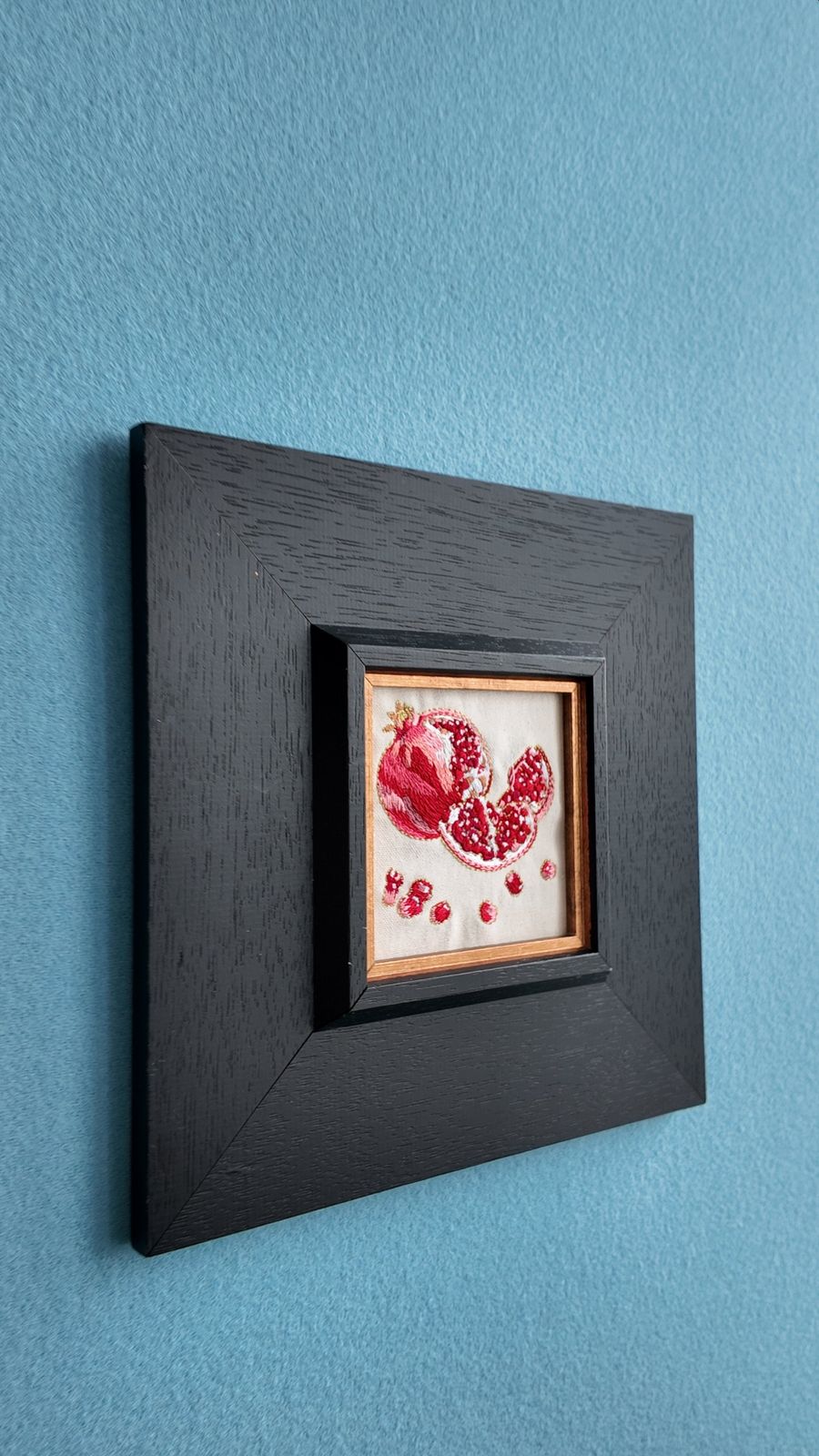 Side view of square pomegranate embroidery wall art in a black wood frame