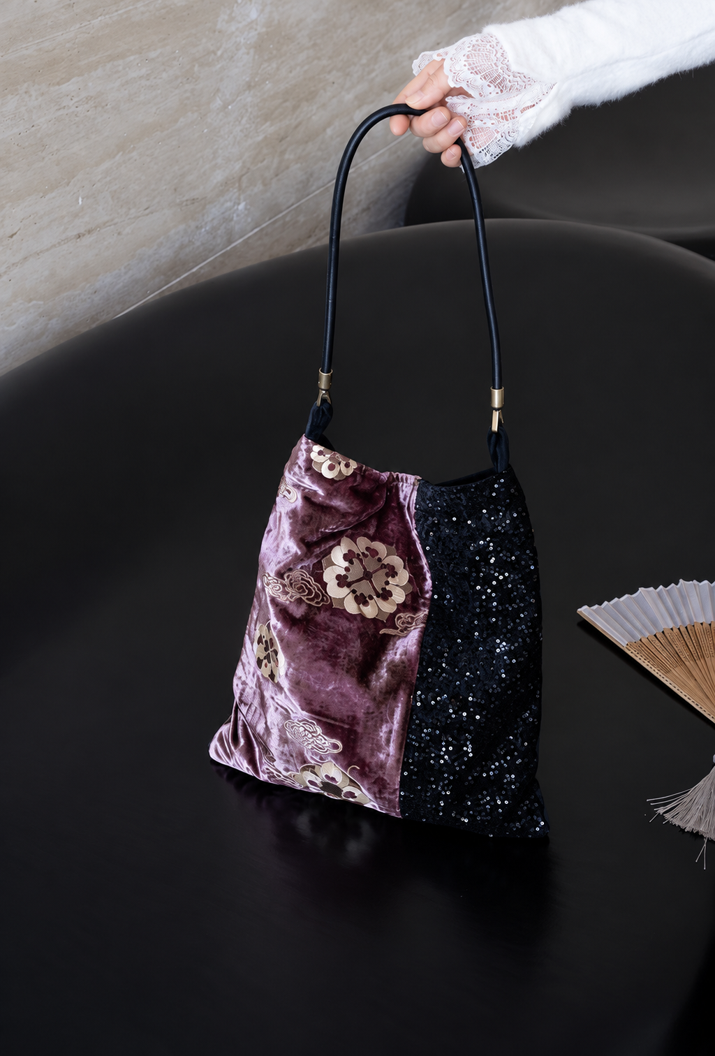 Purple floral velvet and black sequin shoulder bag shown by its long black strap.