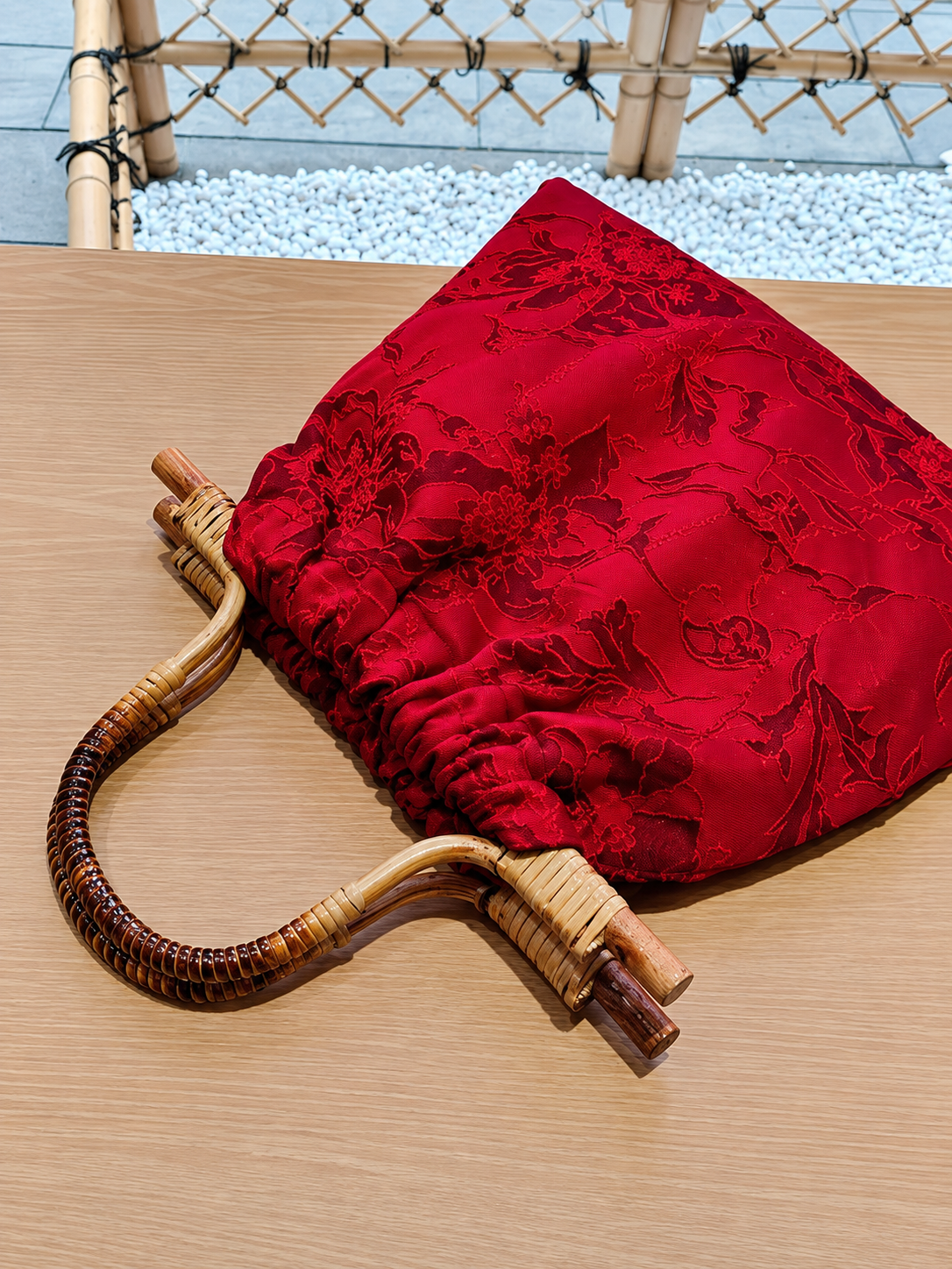 Red floral jacquard bamboo-handle bag displayed beside a window and red lanterns.