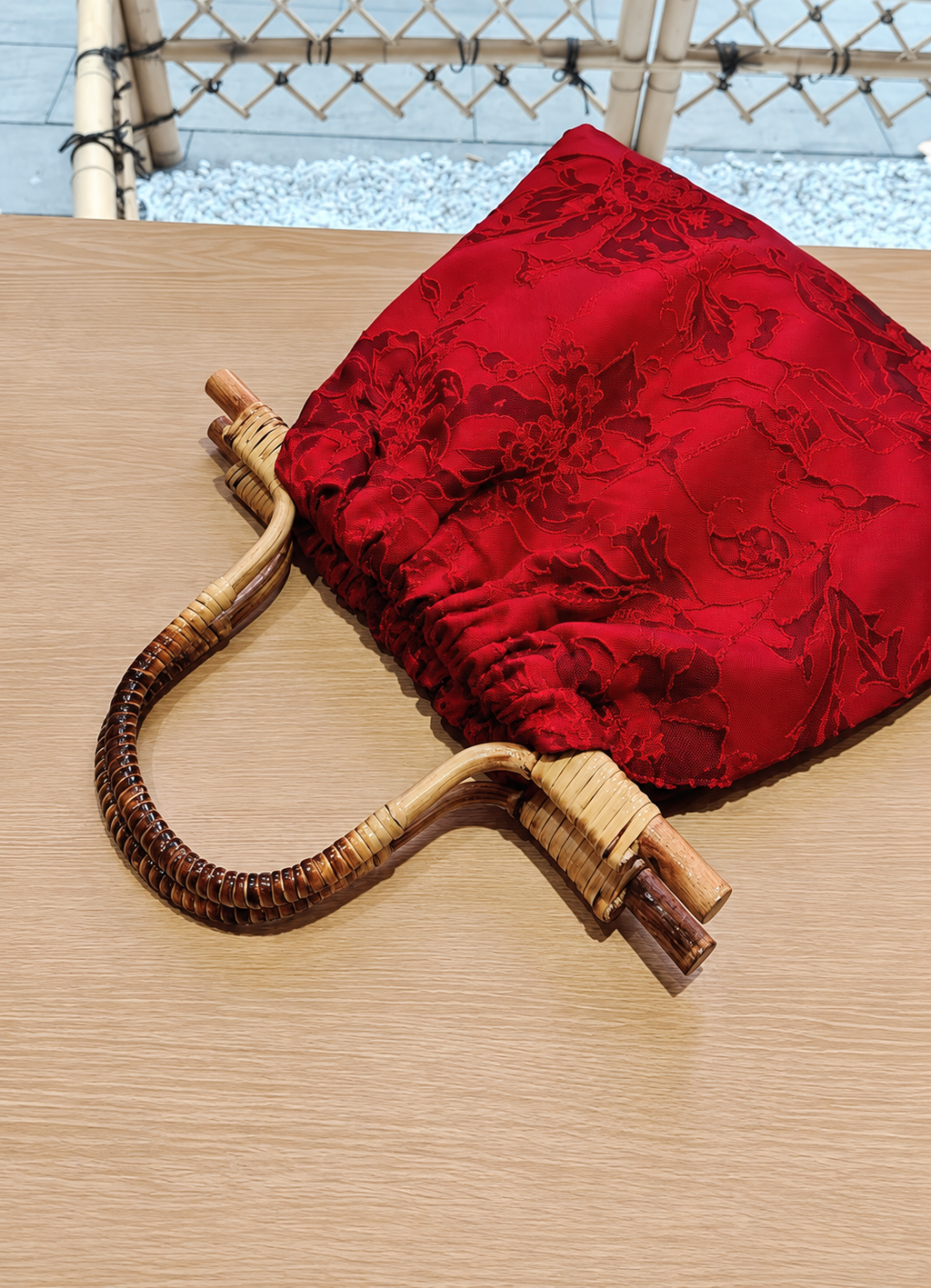 Close-up of glossy red floral jacquard fabric and natural hand-woven bamboo handle.