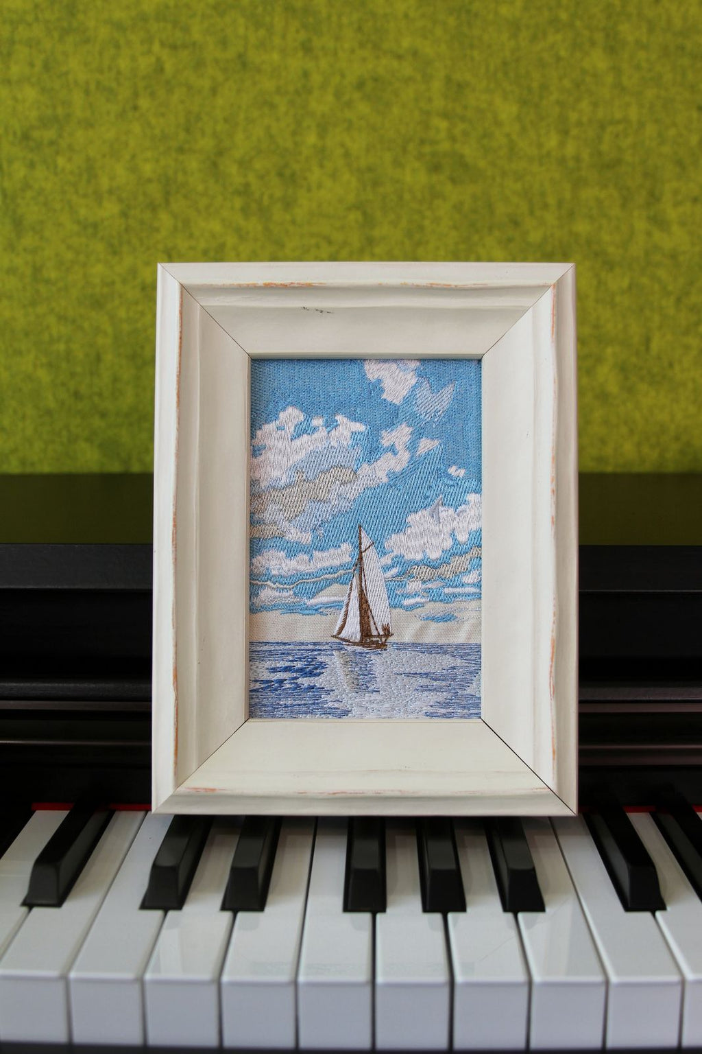 Sail Into the Blue framed sailboat embroidery displayed on a piano