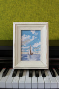 Sail Into the Blue framed sailboat embroidery displayed on a piano