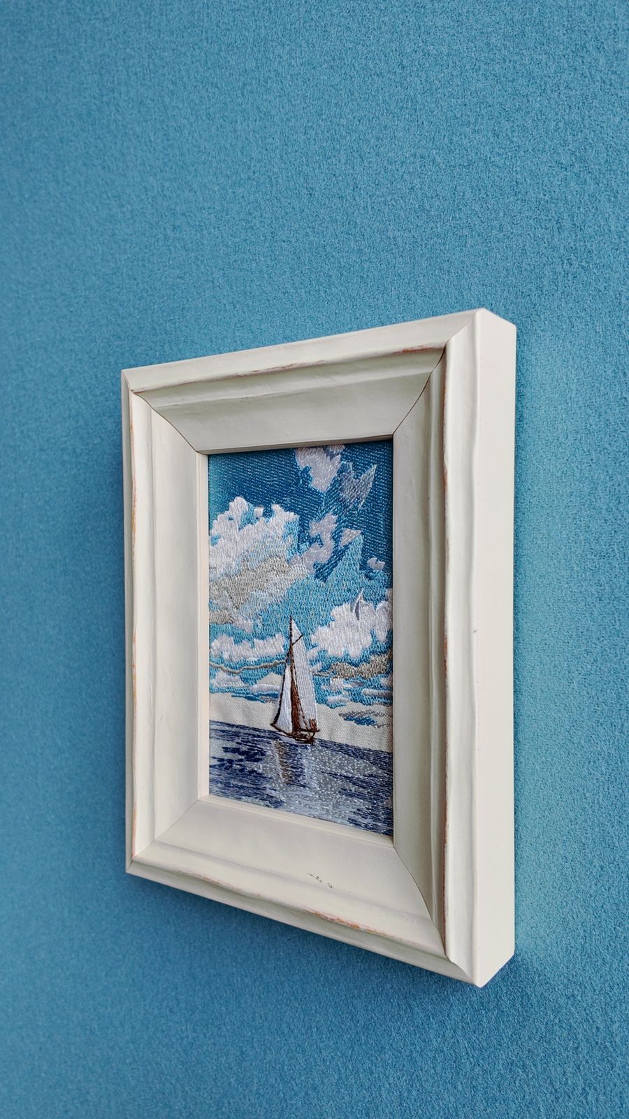 Angled wall view showing the white wooden frame and embroidered sailboat scene