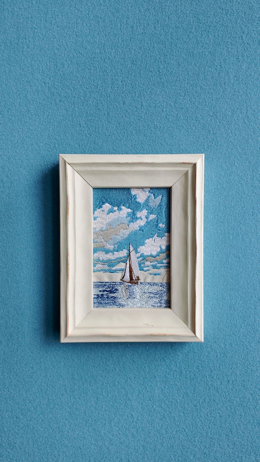 Front wall view of framed sailboat embroidery against a blue wall