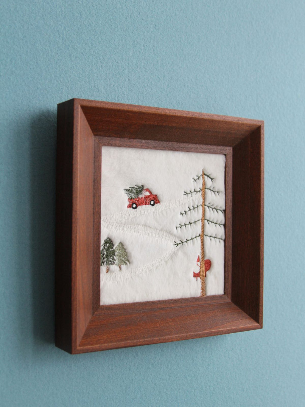Angled close view of velvet Christmas embroidery and brown wood frame