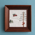 Snowy Christmas embroidered wall art in a square brown wood frame, front view