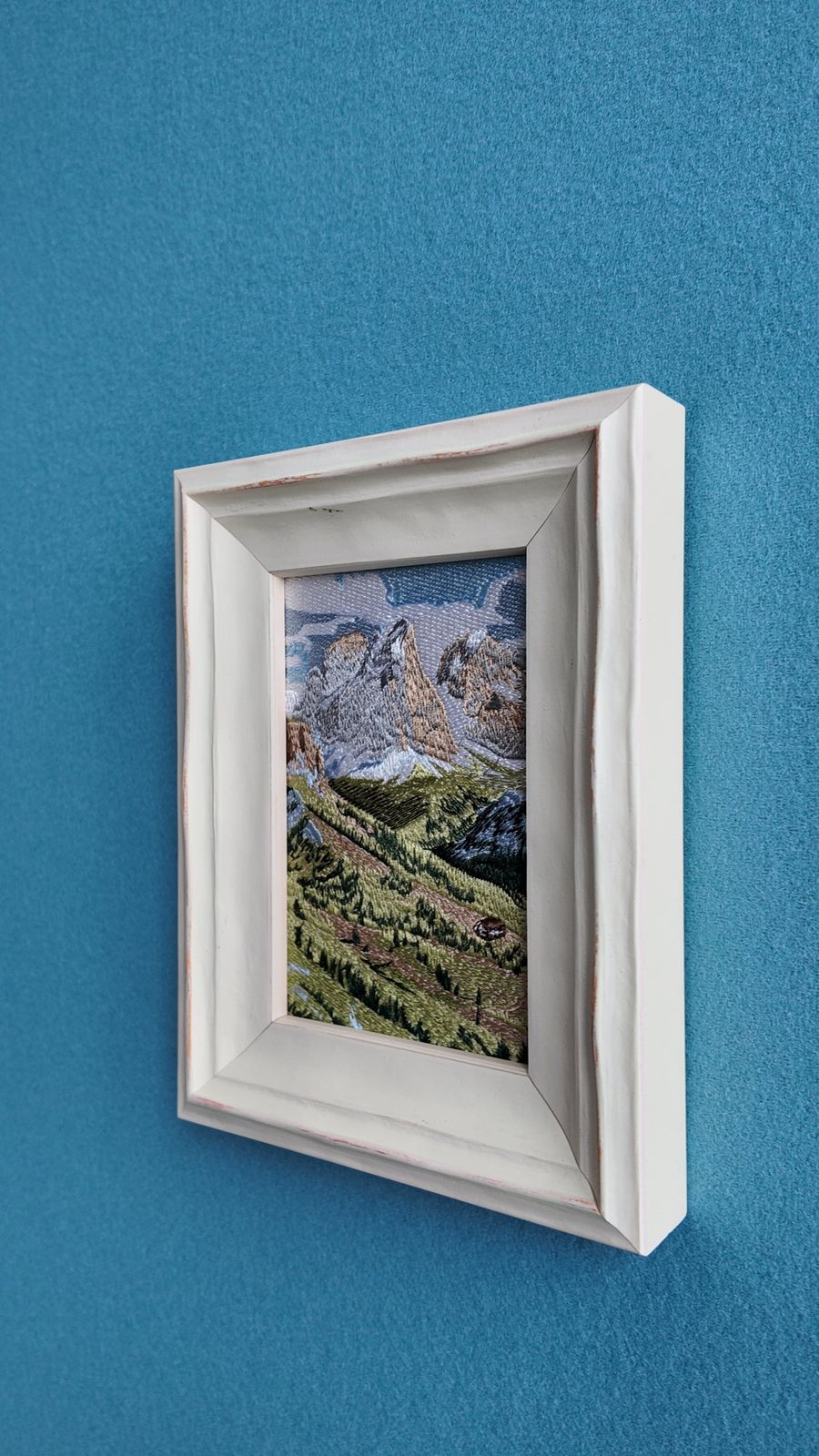 Angled wall view showing the white wood frame and Swiss mountain embroidery