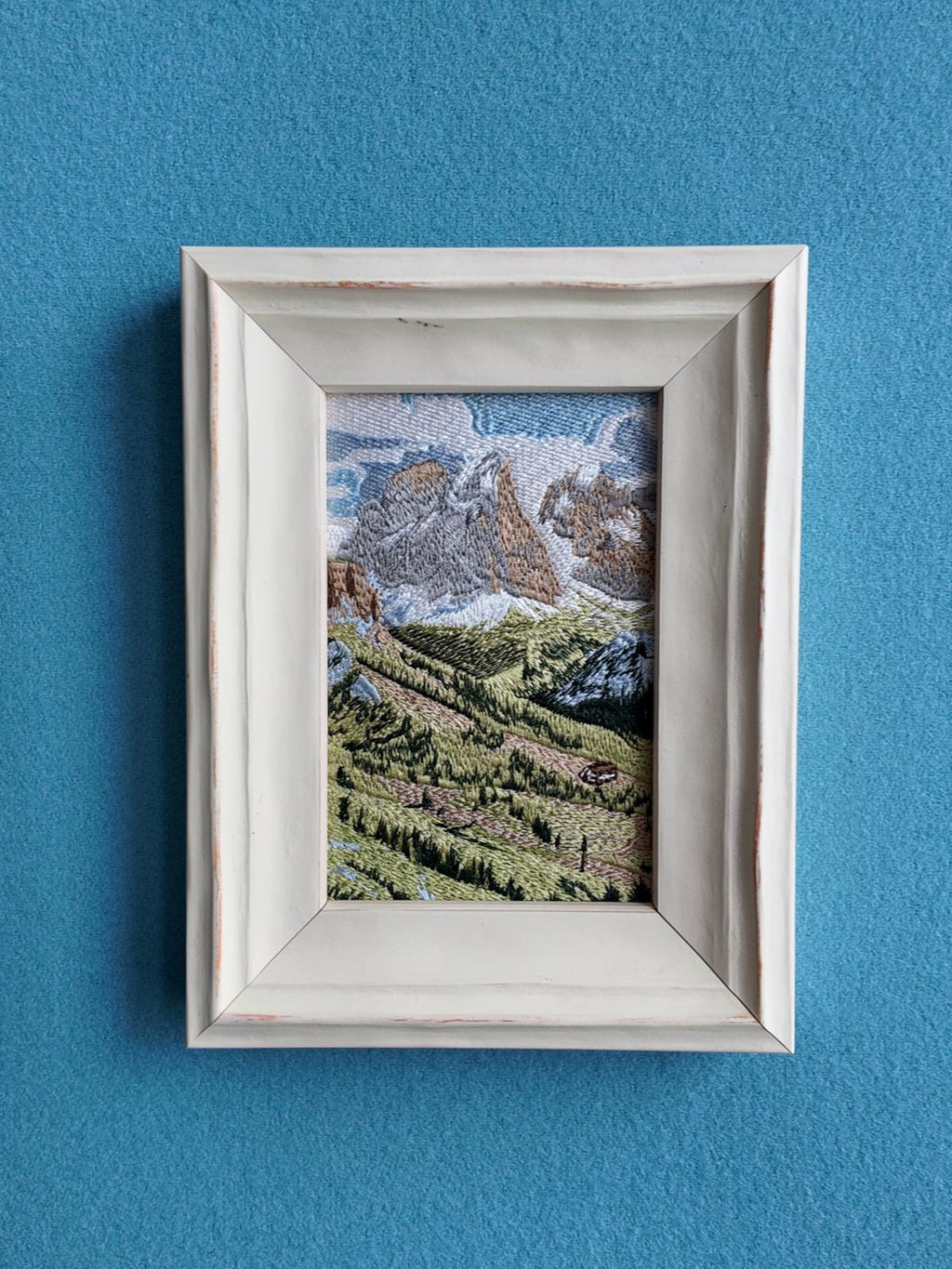 Front wall view of framed Swiss Alps embroidery against a blue wall