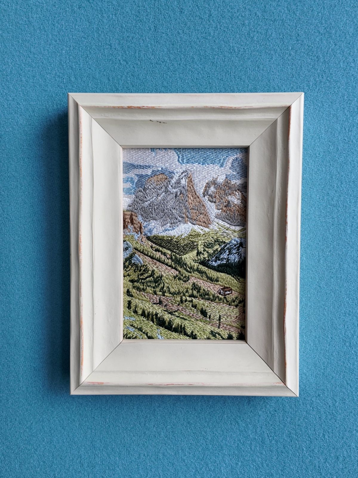 Front wall view of framed Swiss Alps embroidery against a blue wall