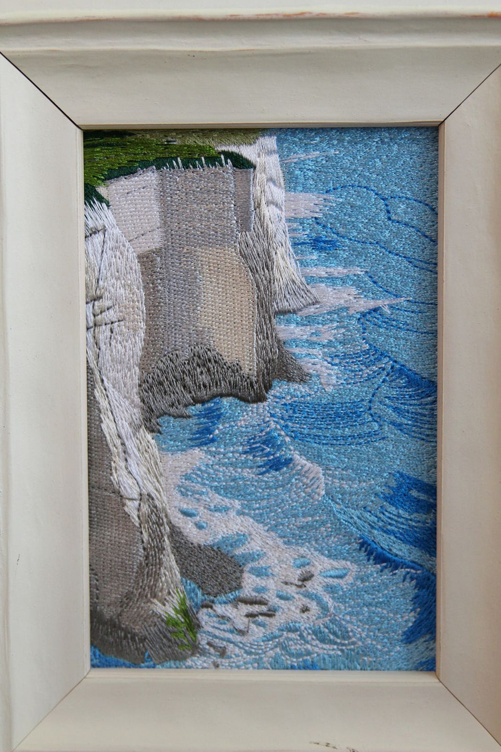 Macro detail of layered blue waves and white cliffs rendered in embroidery