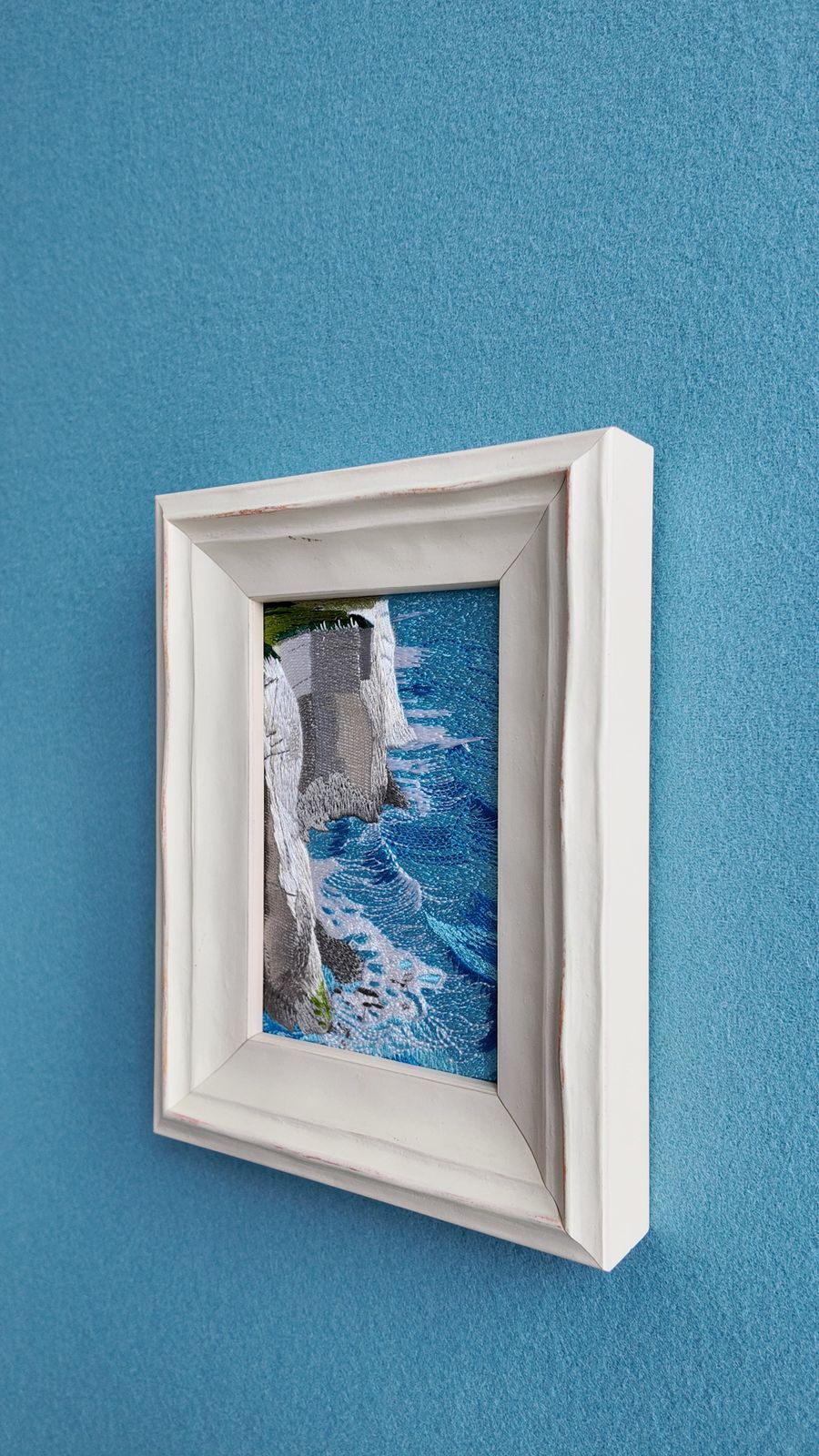 Close angled view of White Cliffs coastal embroidery in a white wooden frame