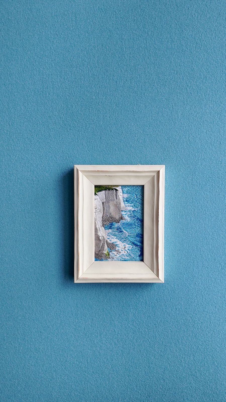 Front view of White Cliffs framed coastal embroidery on a blue wall